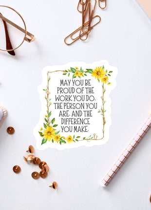 a sticker with a motivational quote, surrounded by various office supplies such as pens, a notebook, and a pair of glasses.