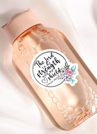 A pink bottle with a label that says "The Lord is strong and powerful" and has a floral design.