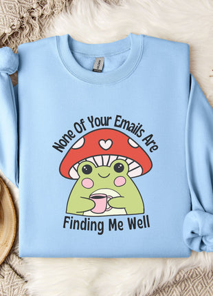 a light blue sweatshirt with a cartoon frog wearing a red mushroom hat and holding a cup, accompanied by the text " none of your emails are finding me well".
