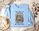 A light blue sweatshirt with a printed design of a cat surrounded by books and a cup of coffee, along with text that reads "Thats what I do I read books I drink coffee and I know things".