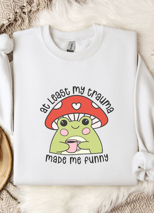 A white sweatshirt with a mushroom character and text printed on it, placed on a bed with a white blanket and a mug.