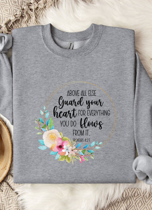 a gray sweatshirt with a floral design and text printed on it, along with a mug and some cotton balls on a bed.