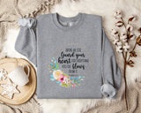 a gray sweatshirt with a floral design and text printed on it, along with a mug and some cotton balls on a bed.