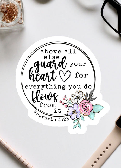 a sticker with a Bible verse and a floral design, surrounded by various office supplies such as a watch, pen, and glasses.