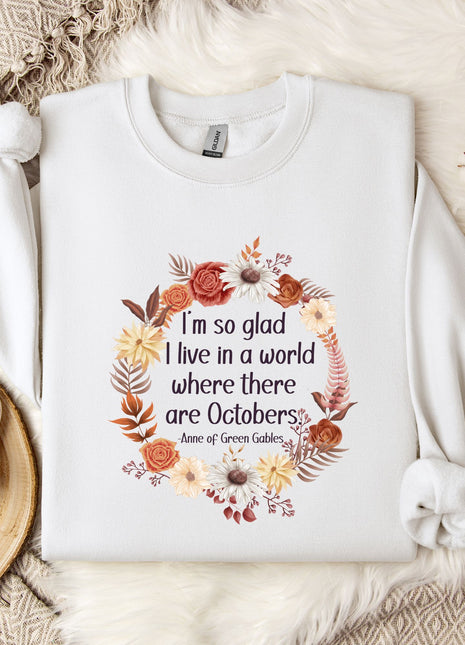 A white sweatshirt with a floral design and text printed on it, placed on a bed with a white blanket and a mug.