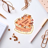 a heart-shaped sticker with the text "Autumn Girl" and various autumn-themed elements, such as pumpkins and bows, surrounding it. The sticker is placed on a white surface, along with a pair of glasses, a pen, a notebook, and some office supplies like a stapler and a pen holder.
