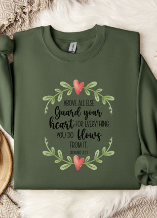 a green sweatshirt with a printed message, a white mug, and some white flowers on a bed with a white blanket.