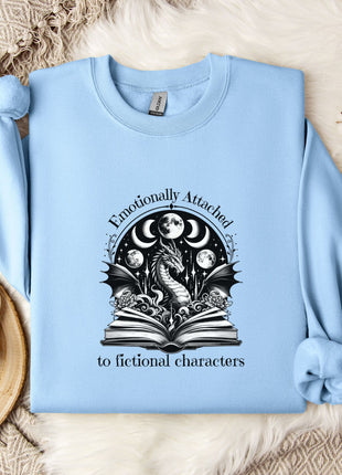 A light blue sweatshirt with a graphic design on it, along with a mug, a plant, and some flowers, all placed on a white fur rug.