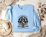 A light blue sweatshirt with a graphic design on it, along with a mug, a plant, and some flowers, all placed on a white fur rug.