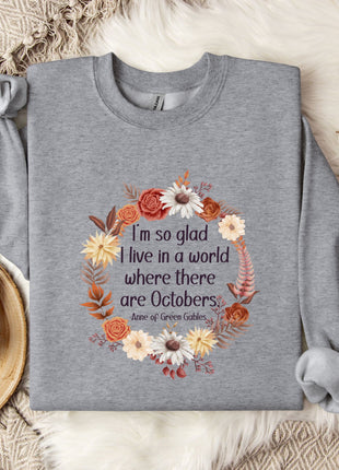 A gray sweatshirt with a floral wreath design and a quote printed on it, placed on a beige blanket with a white mug and a branch of cotton balls nearby.
