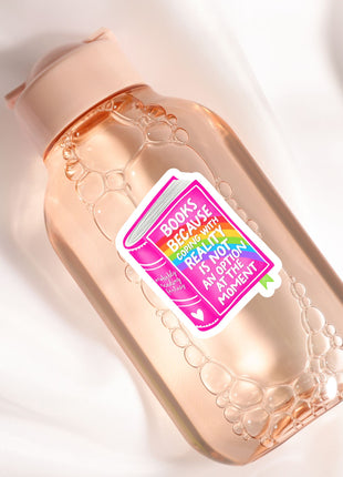 A pink bottle with a sticker that says "Books because reality is optional" and has a rainbow design.