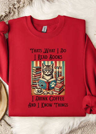 A red sweater with a printed design of a cat surrounded by books and a cup of coffee, along with the text "Thats What I Do I Read Books I Drink Coffee and I Know Things".