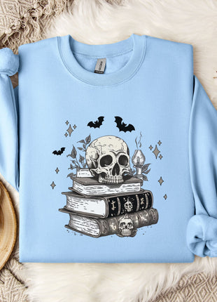 a light blue sweatshirt with a skull and bat design on it, along with a stack of books and some white flowers.