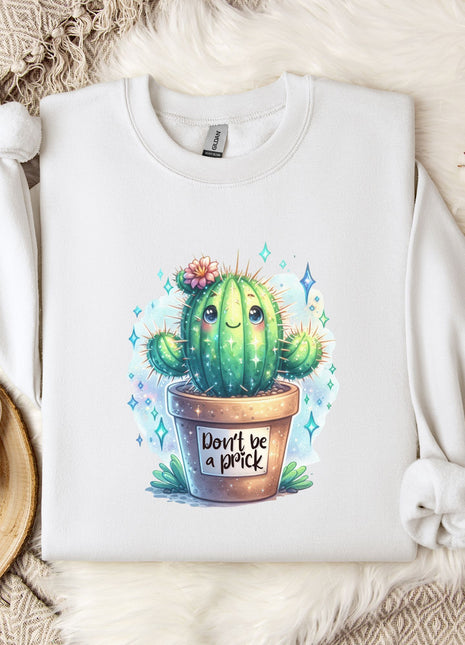 a white sweatshirt with a colorful illustration of a cactus on it, along with a mug and some decorative elements such as a snowflake and a branch of cotton flowers.