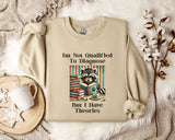 a beige sweatshirt with a graphic design of a raccoon surrounded by books and a cup of coffee, along with text that reads "I'm Not Qualified To Diagnose But I Have Theories".