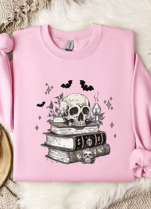 A pink sweatshirt with a skull and bat design, along with a stack of books and a mug, is displayed on a white fur rug.