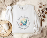 A white sweatshirt with a colorful graphic of a seashell and starfish, along with the text "And to the beach go, to lose and to love again" printed on it, is displayed on a bed with a white blanket and a mug.