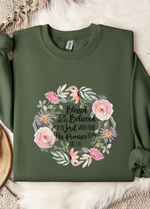 A green sweatshirt with a floral design and text printed on it, along with a mug, a white mug, and some white flowers on a white surface.