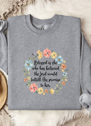 A gray sweatshirt with a floral design and text printed on it, placed on a bed with a white blanket and a white mug.