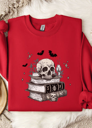 a red sweater with a skull and bat design, along with a stack of books and a mug, all placed on a white fur rug.