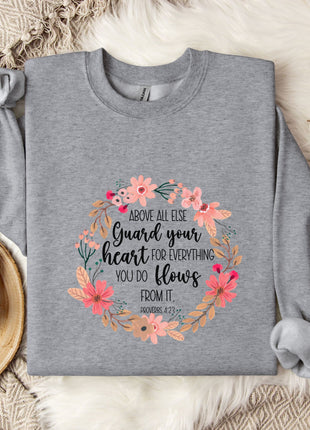 a gray sweatshirt with a floral design and text printed on it, along with a mug and some cotton balls on a bed.