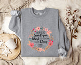 a gray sweatshirt with a floral design and text printed on it, along with a mug and some cotton balls on a bed.