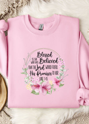A pink sweatshirt with a floral design and text printed on it, placed on a white fur rug.