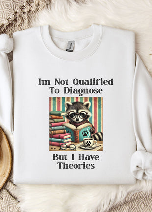 a white t-shirt with a graphic design of a raccoon wearing glasses and surrounded by books, along with text that reads "I'm Not Qualified To Diagnose But I Have Theories".