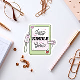a sticker with the text "Lazy Kindle Girlie" surrounded by various office supplies such as a pen, a pair of glasses, and a notebook.