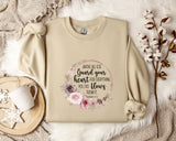 a beige sweatshirt with a floral design and text printed on it, along with a coffee mug and some decorative elements such as a snowflake and a branch.