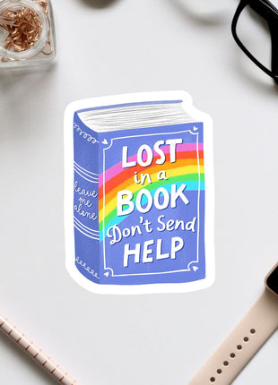 a sticker with a book and a rainbow, along with some office supplies such as a pen, a watch, and a pair of glasses.