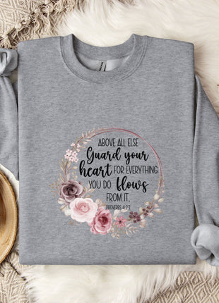 a gray sweatshirt with a floral design and text printed on it, placed on a bed with a white blanket and a mug.