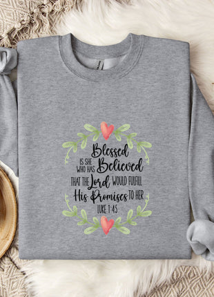 A gray sweatshirt with a Bible verse printed on it, along with a mug, a branch of cotton flowers, and a wooden tray.