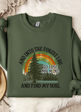 A green sweatshirt with a graphic design and text printed on it, placed on a bed with a white blanket and a white mug.