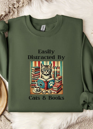 a green sweatshirt with a printed design of a cat surrounded by books, along with the text "Easily Distracted By Cats & Books".