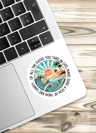 A sticker with a beach scene and a quote is placed on the edge of a laptop keyboard.