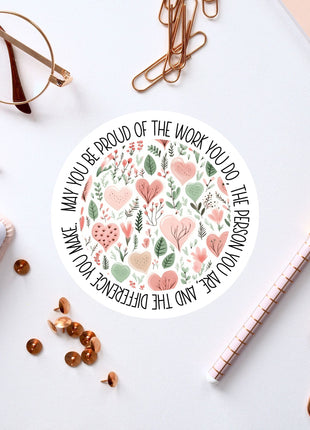 a white circular sticker with a floral design, surrounded by various office supplies such as pens, a pair of glasses, and a notebook.