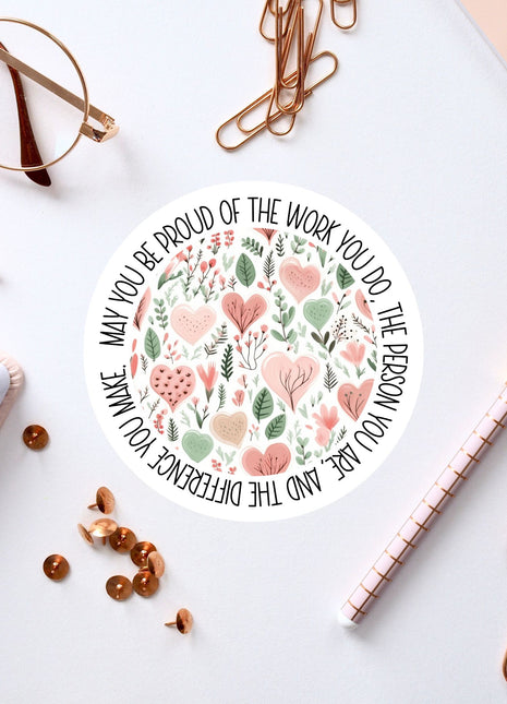 a white circular sticker with a floral design, surrounded by various office supplies such as pens, a pair of glasses, and a notebook.
