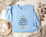 A light blue sweatshirt with a printed design and text, placed on a bed with a white blanket and a white mug with a heart design.