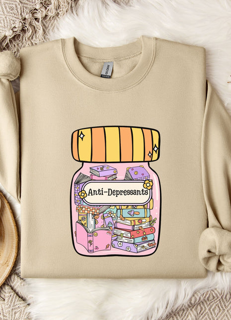 a beige sweatshirt with a colorful graphic design depicting a jar with various objects inside, including a book and a flower. The sweatshirt is placed on a bed with a white blanket and a white mug with a heart design.
