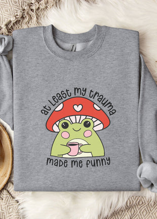 A gray sweatshirt with a mushroom graphic and text, along with a mug and some white flowers, all placed on a beige blanket.