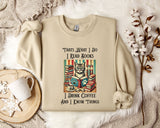A beige sweatshirt with a printed design of a cat surrounded by books and a cup of coffee, along with the text "Thats What I Do I Read Books I Drink Coffee and I Know Things".