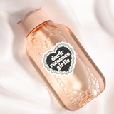A pink bottle with a black heart-shaped label that says "Dark Romance Girlie" on it.