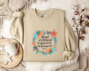 A beige sweatshirt with a floral design and text printed on it, along with a mug, a branch of cotton flowers, and a wooden tray with snowflakes on it, all arranged on a white fur rug.