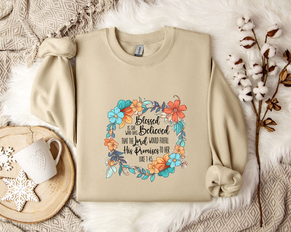A beige sweatshirt with a floral design and text printed on it, along with a mug, a branch of cotton flowers, and a wooden tray with snowflakes on it, all arranged on a white fur rug.