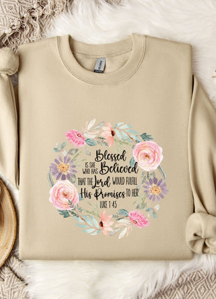 A beige sweatshirt with a floral design and text printed on it, along with a mug, a branch of cotton flowers, and a wooden tray.