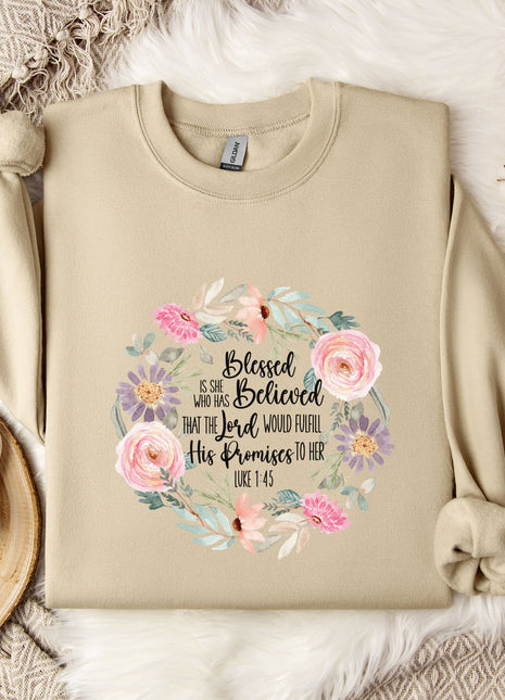 A beige sweatshirt with a floral design and text printed on it, along with a mug, a branch of cotton flowers, and a wooden tray.