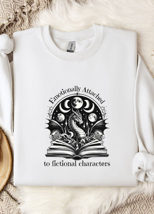 a white sweatshirt with a graphic design on it, placed on a bed with a white blanket and a mug.