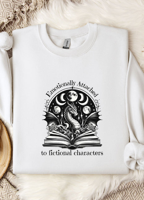 a white sweatshirt with a graphic design on it, placed on a bed with a white blanket and a mug.
