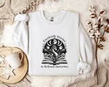 a white sweatshirt with a graphic design on it, placed on a bed with a white blanket and a mug.
